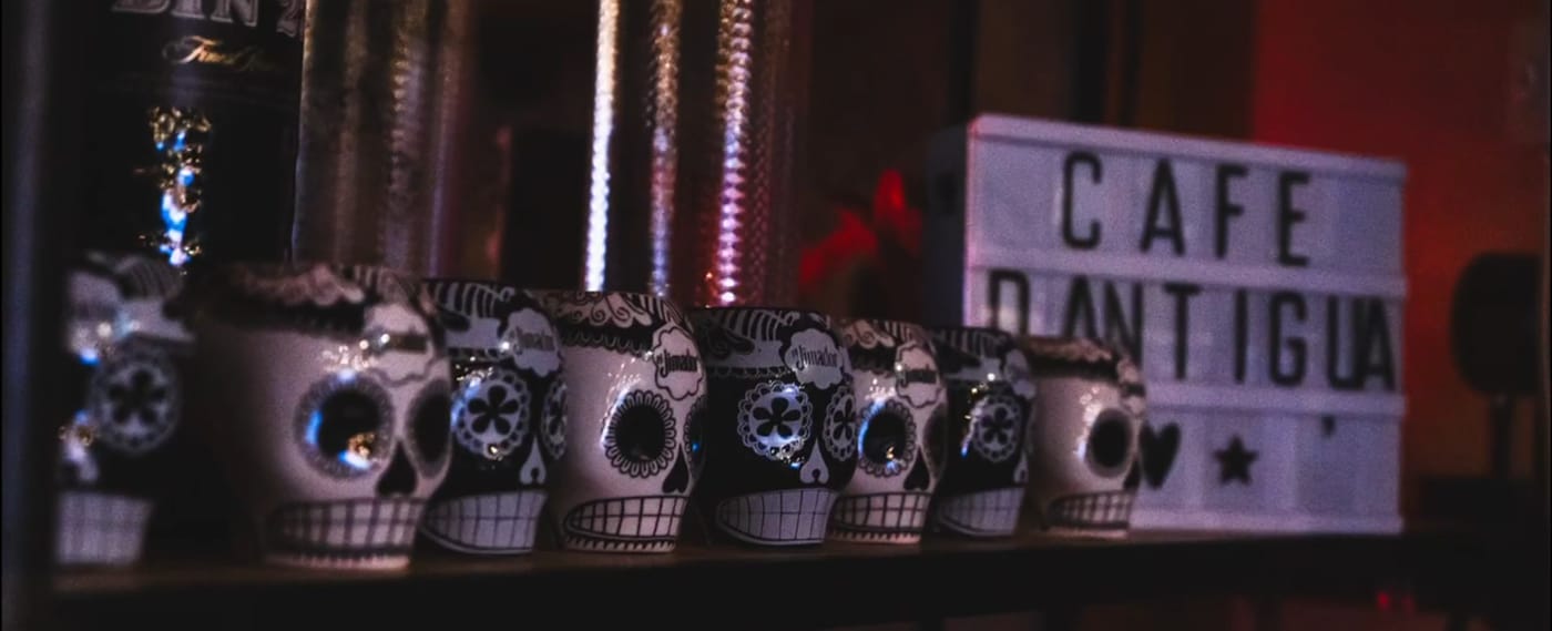A lit sign reading Cafe D'Antigua on a shelf behind the bar